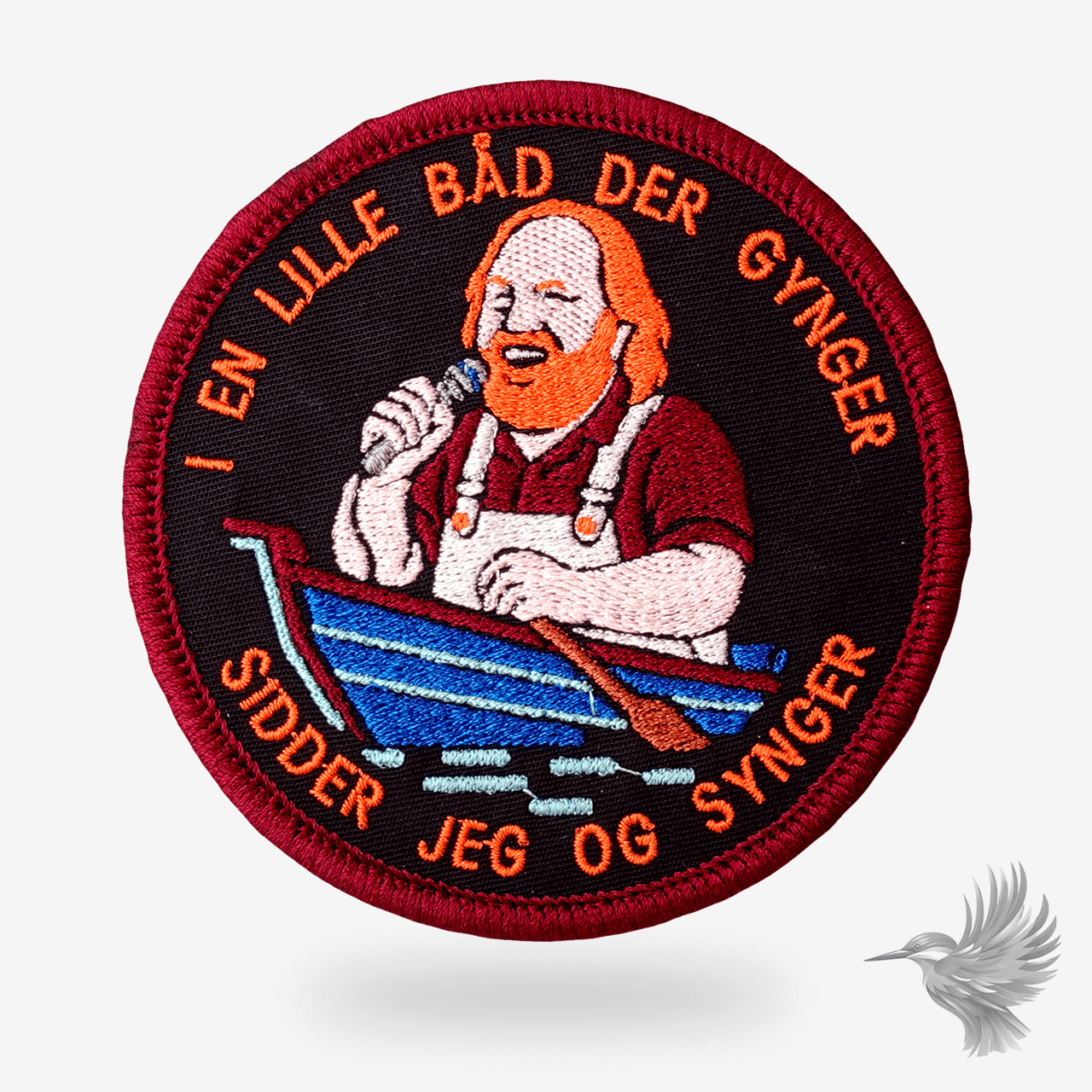 Rundt broderet patch med Flemming “Bamse” Jørgensen syngende i en blå rød-stribet robåd med teksten “I en lille båd der gynger, sidder jeg og synger”