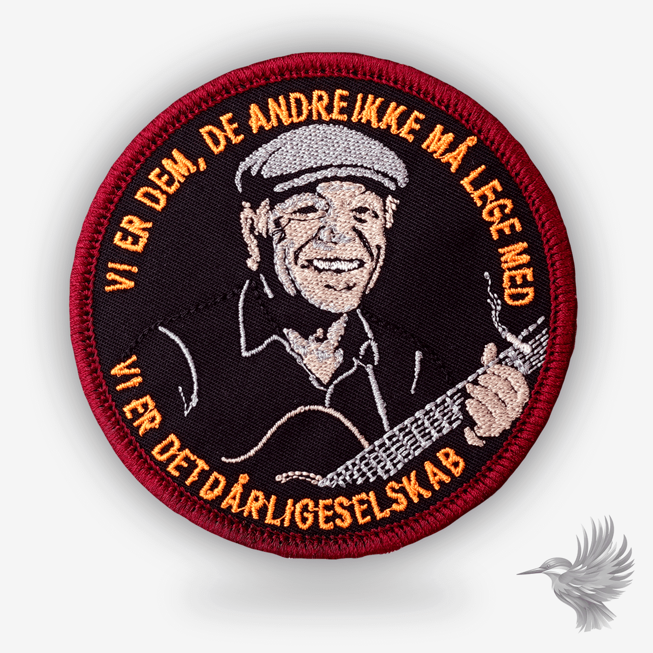 Rundt broderet patch med portræt af Kim Larsen og teksten “Vi er dem de andre ikke må lege med – vi er det dårlige selskab” i orange og rød