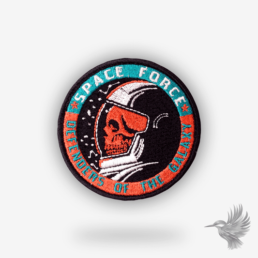 Broderet rundt patch med død astronaut i hjelm og teksten “Space Force – Defenders of the Galaxy” i blå og orange