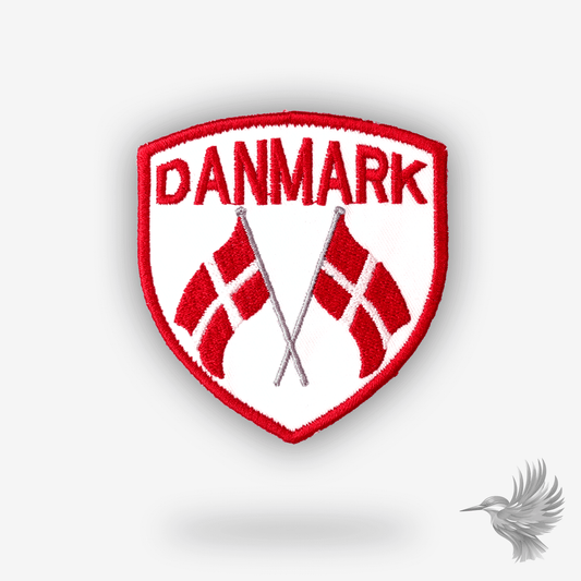 Broderet mærke formet som skjold med teksten “Danmark” og to krydsede dannebrogsflag i rød og hvid