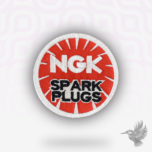 NGK Spark Plugs patch strygemærke med rød baggrund og hvitt logo, symbol på motorsport og mekanisk perfektion.