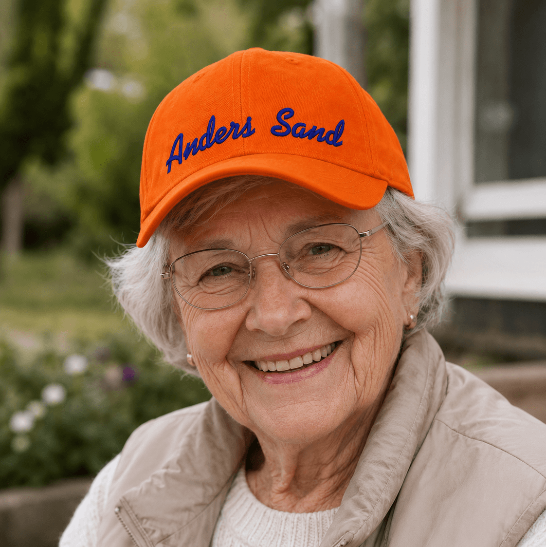 Orange CAP Kasket med Egen Tekst og Broderi på en smilende ældre kvinde med briller.